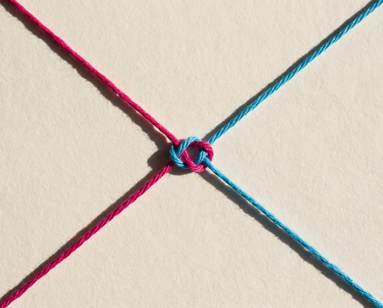Een magenta en een cyaan draad uit tegenoverliggende hoeken, in het midden verbonden met een nette knoop