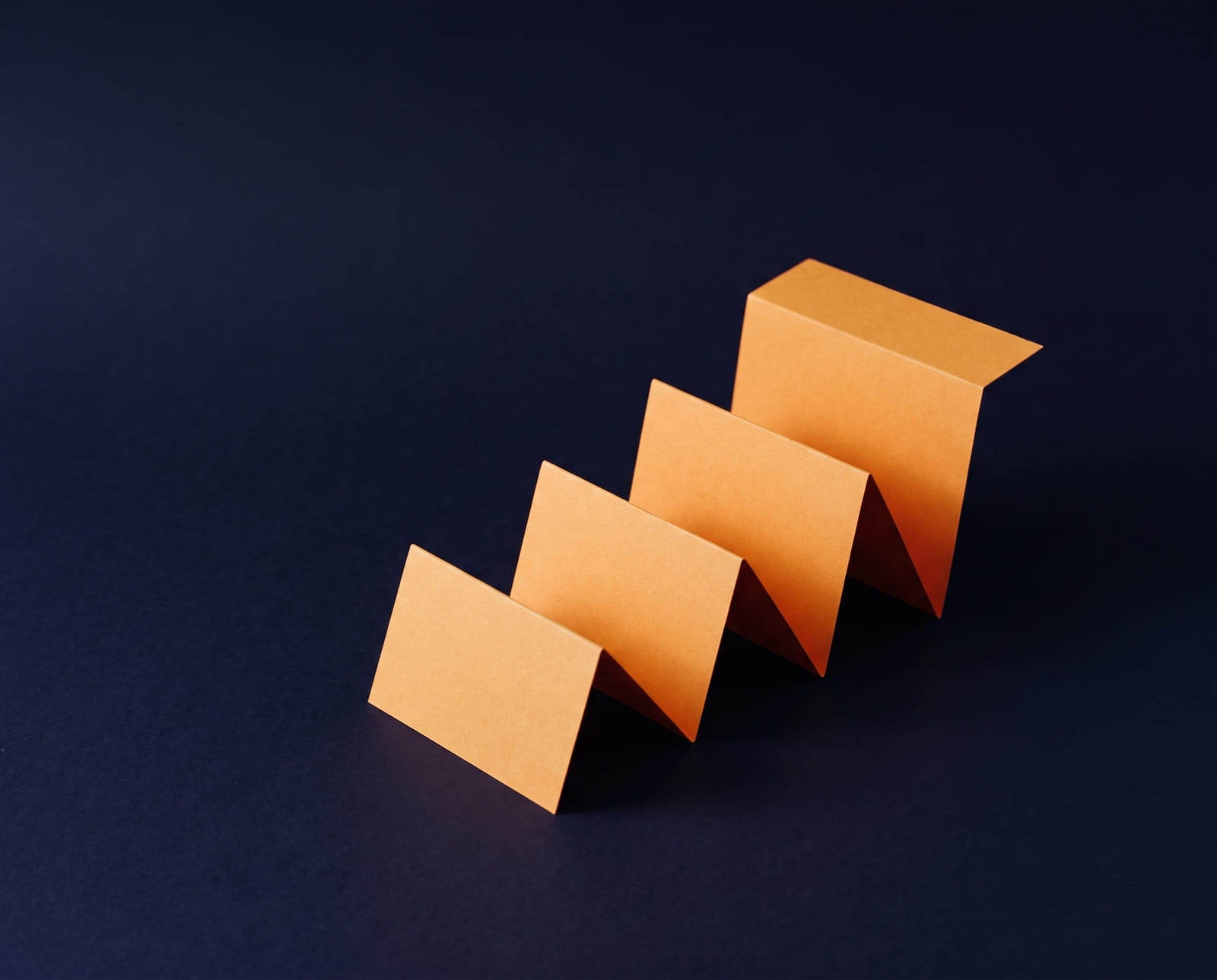 Een oranje kartonnen trap van vier treden, gevouwen uit één stuk, op donker indigo